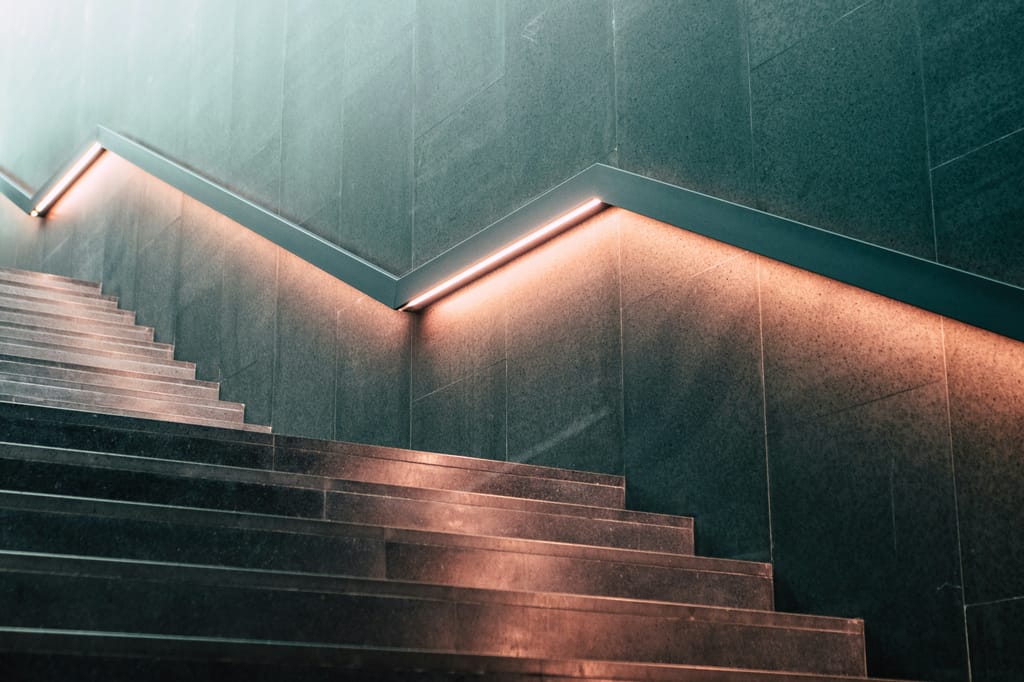 Lit staircase rising along a concrete wall