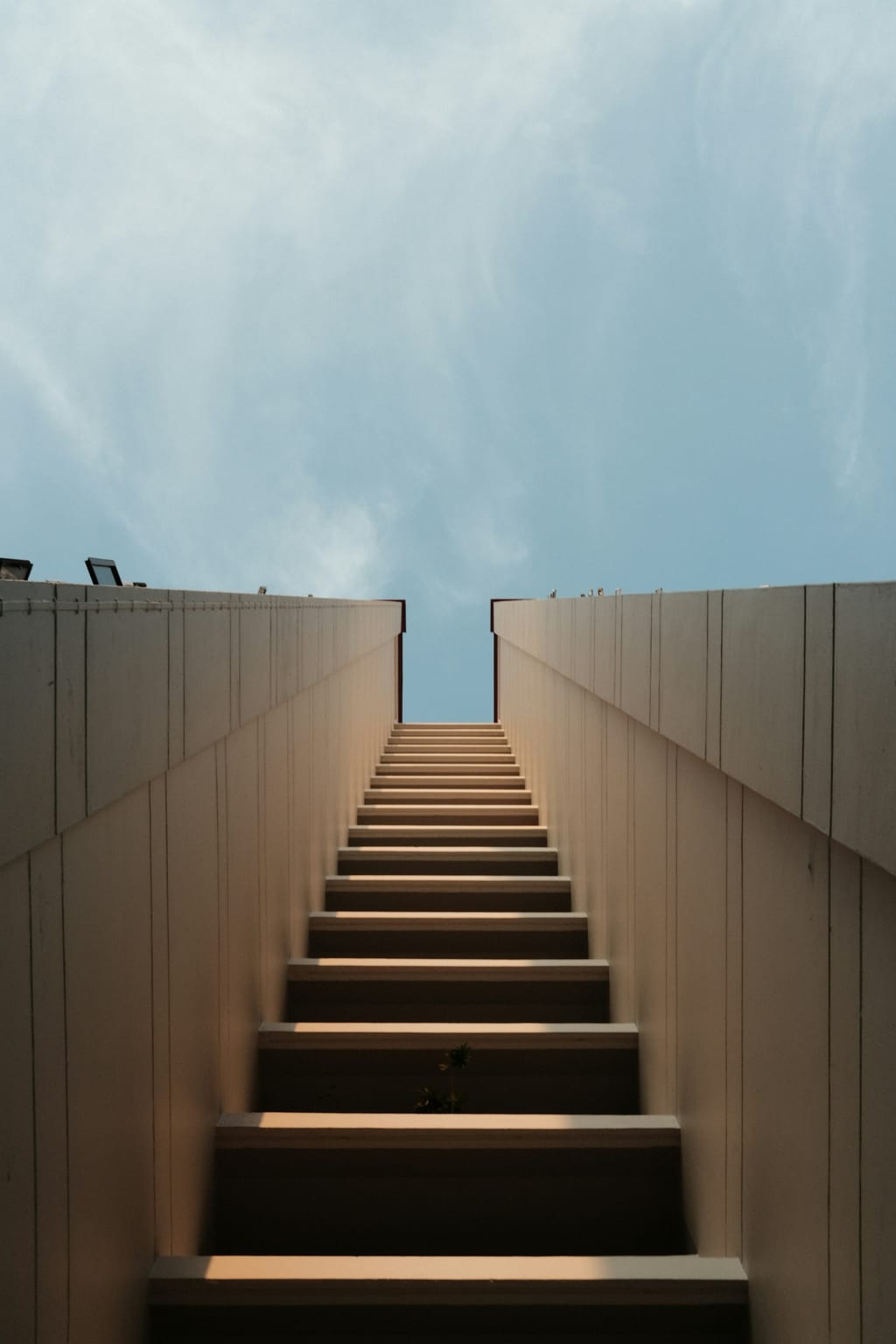 A staircase between two walls climbing toward the open sky